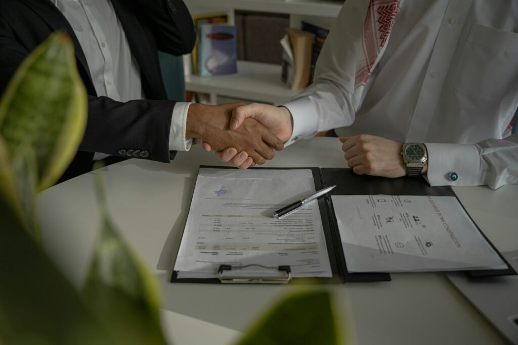 Two people shaking hands across a desk of documents